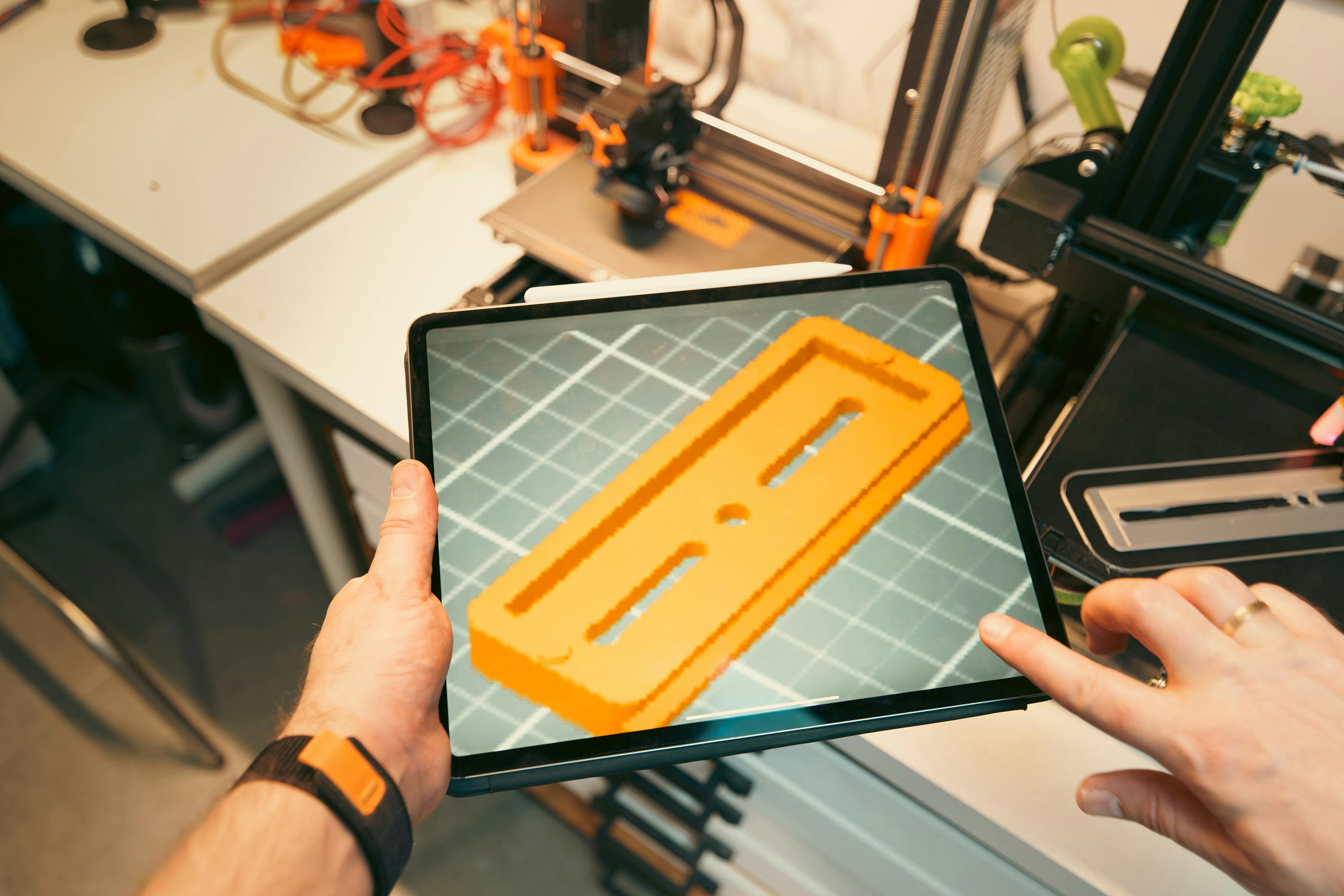 Reviewing a 3D part design on a tablet with FDM printers running in the background